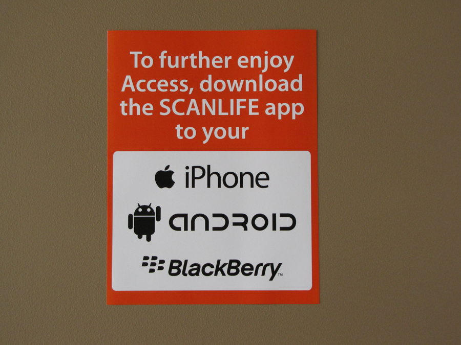 A printed sign on an orange background instructing gallery visitors to download the SCANLIFE app on their iPhone, Android, or BlackBerry to interact with the exhibition.