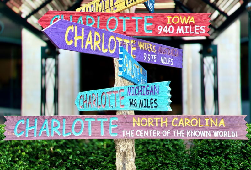 A colorful directional sign post in Charlotte, North Carolina pointing to other cities named Charlotte around the world. The bottom sign reads Charlotte North Carolina — The Center of the Known World.